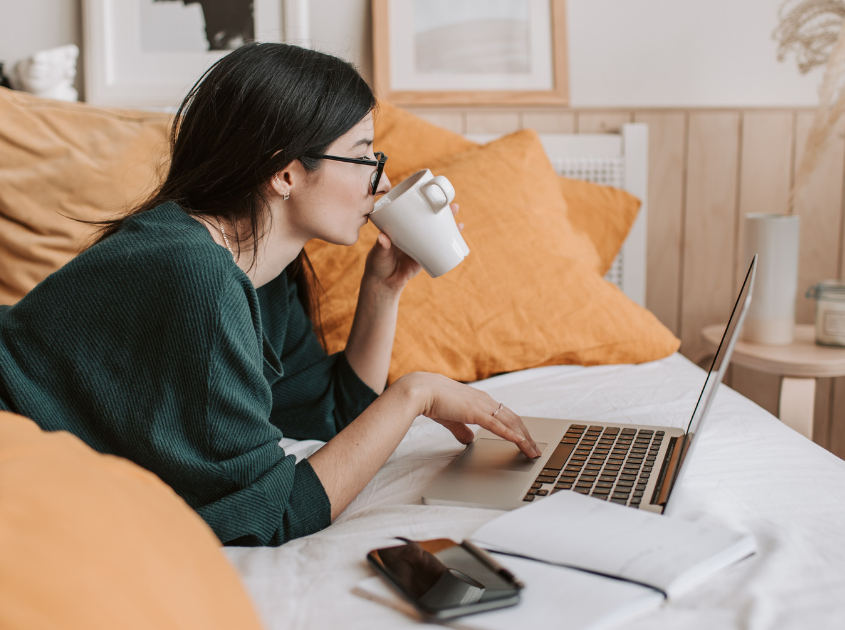 girl laying in bad drinking coffee and working